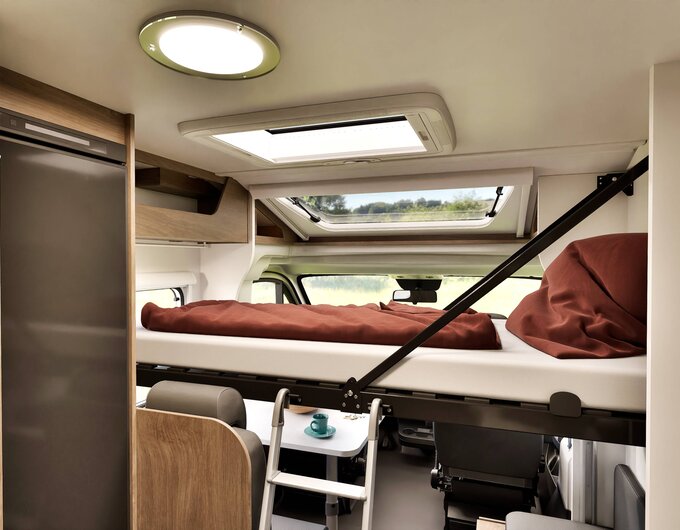 Intérieur d’un camping-car Carado avec lit de pavillon au-dessus de la cabine, échelle, lanterneau et réfrigérateur