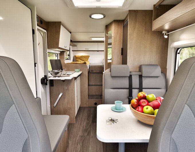 Intérieur du camping-car Carado avec coin salon, table, coupe de fruits, cuisine compacte et lit arrière