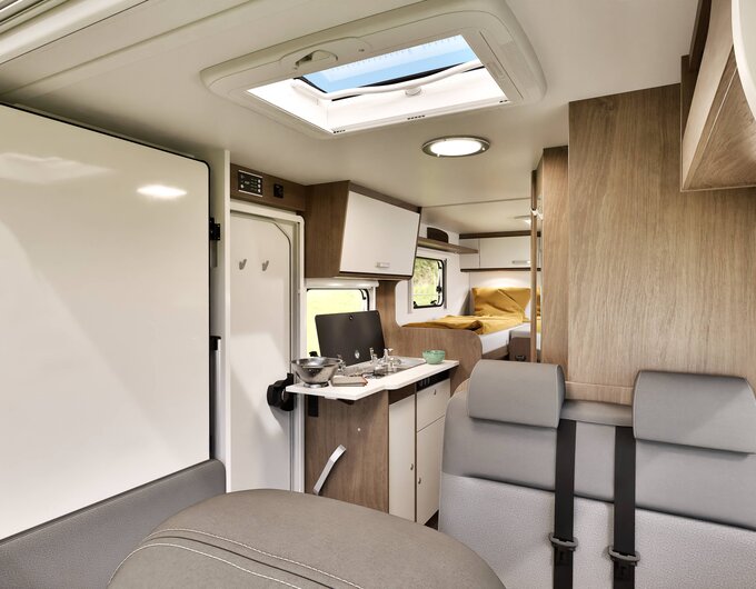 Intérieur du camping-car Carado avec banquette, bloc cuisine, lanterneau de toit et lits simples à l’arrière