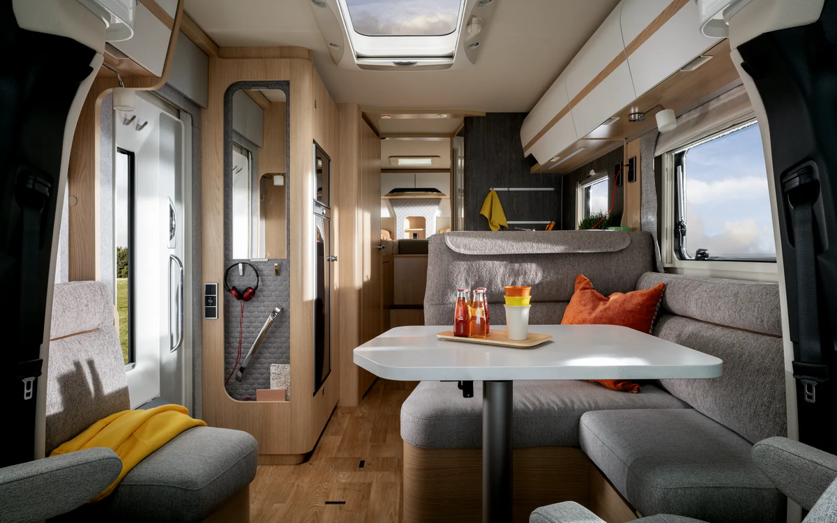 Sideboard-ingangsdeur met koptelefoon en overdekt zitgedeelte met oranje kussens naar achteren in de HYMER B-ML T