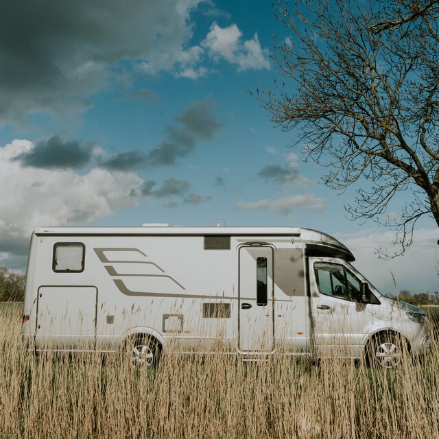 Zijaanzicht van een HYMER-camper onder halfbewolkte hemel in een landelijke omgeving met grassen op de voorgrond