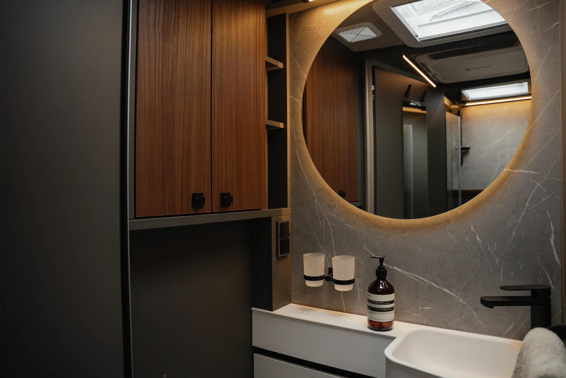 De verlichte ronde spiegel en indirecte sfeerverlichting creëren een atmosfeer die kwaliteit, rust en modern design harmonieus verbindt.
