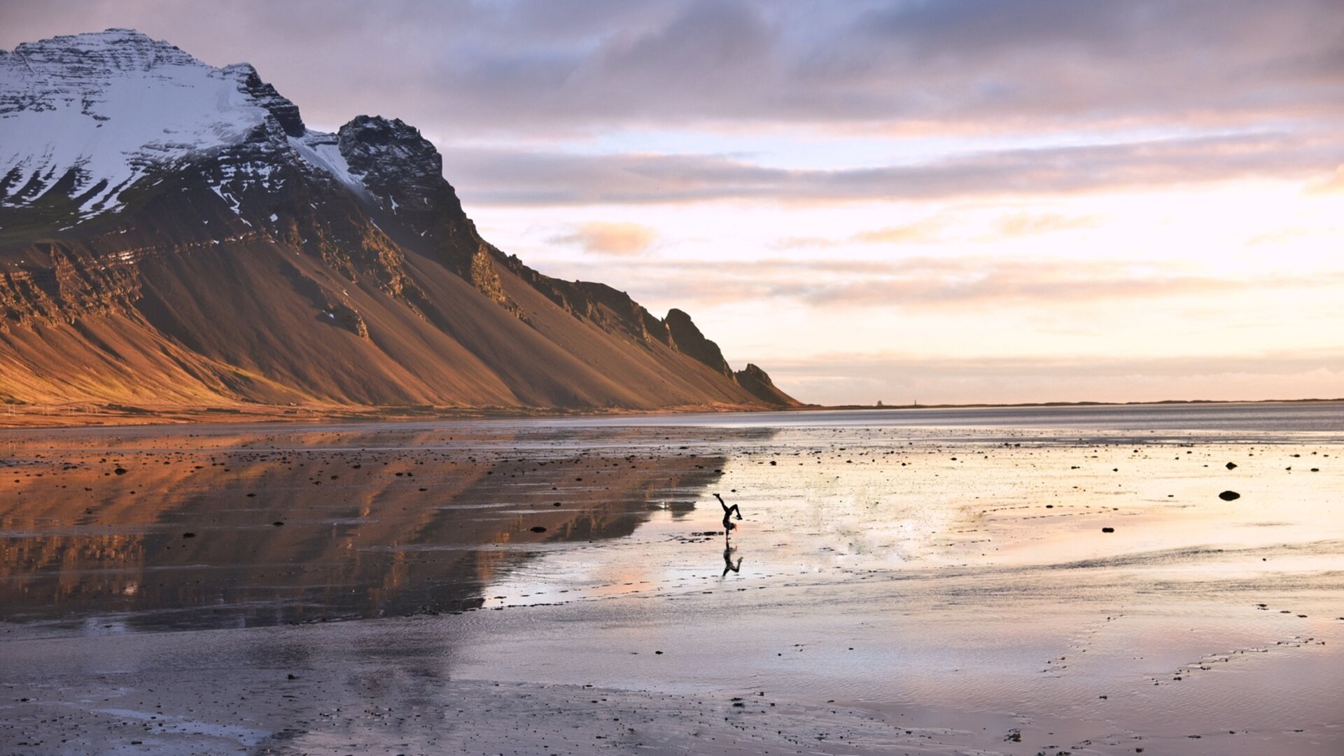 Un paysage reflète le ciel sur une surface humide, avec des montagnes enneigées en arrière-plan. De l'article de voyage "En camping-car en Islande".