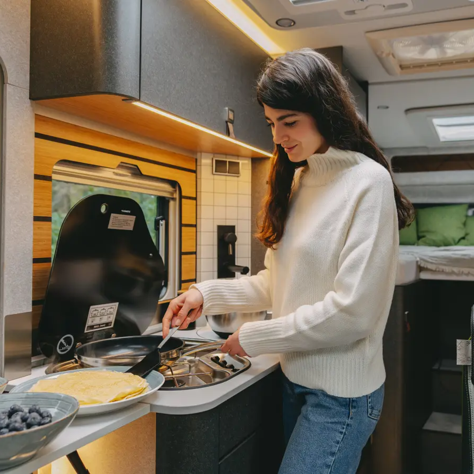 Jonge vrouw die pannenkoeken bereidt in de camperkeuken van een zeer moderne camper