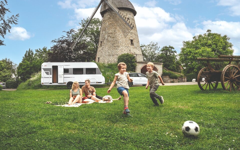 Zwei Kinder spielen vor einem LMC Sassino Wohnwagen Fußball.